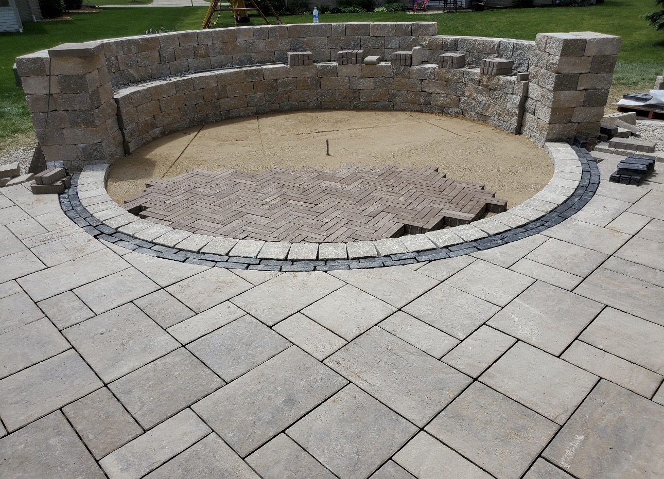 Curved stone seating wall with herringbone brick fire pit floor under construction