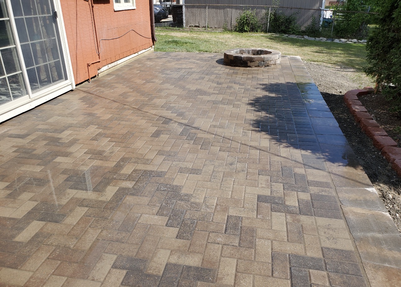 Finished herringbone paver patio with a round stone fire pit in the backyard