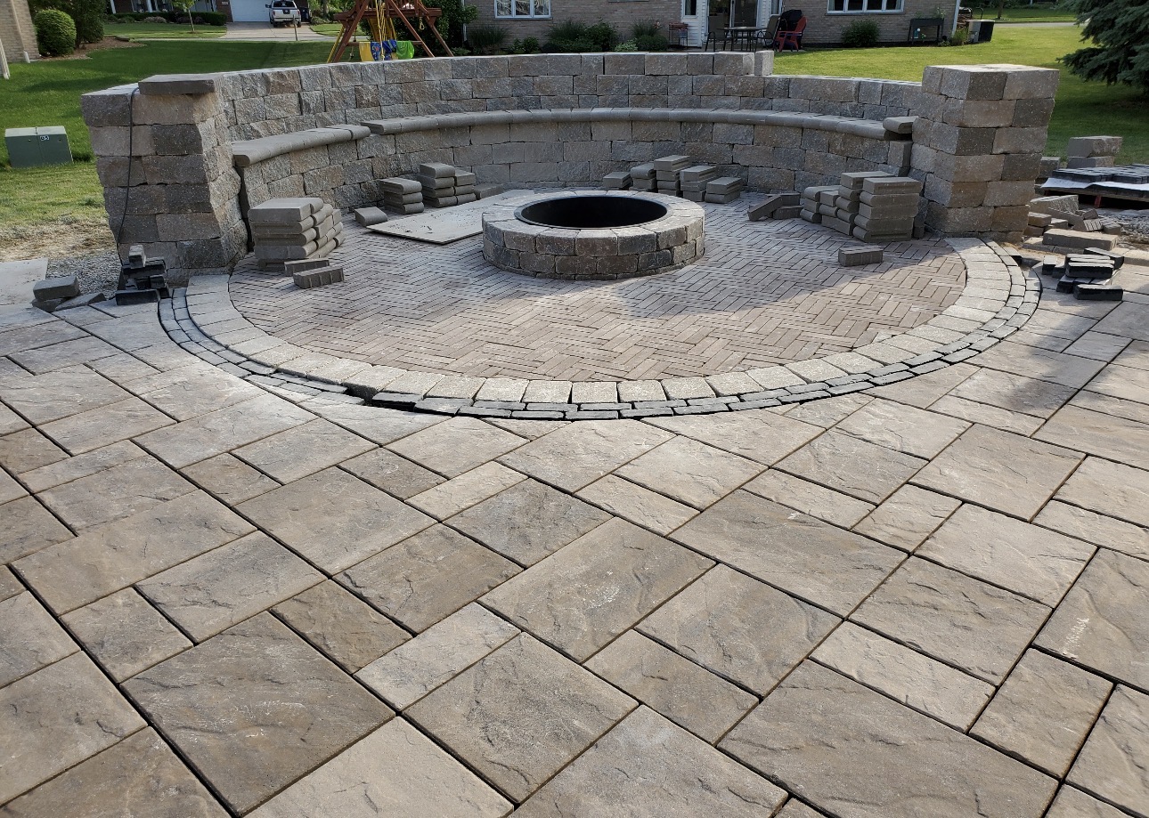Finished paver patio with circular herringbone fire pit inlay and curved stone seating wall