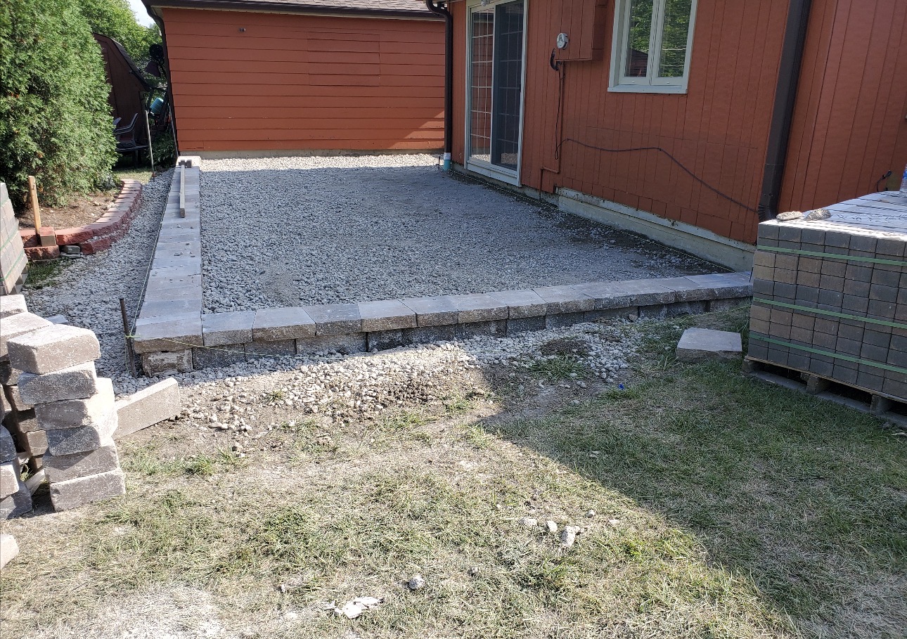 Compacted gravel patio base with edge restraint set behind a red house