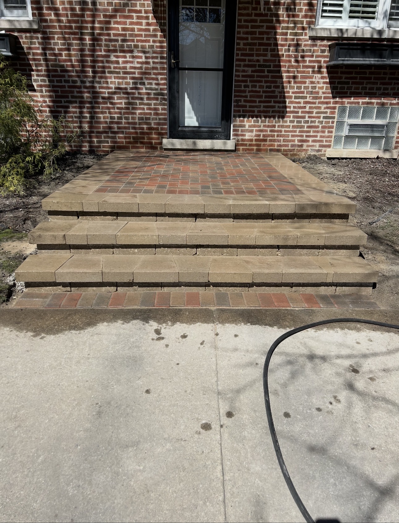 Brick paver front entry stoop with layered steps against a red brick home