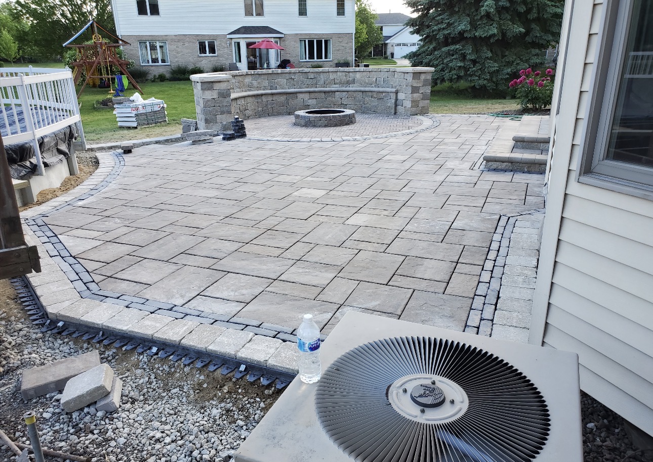 Large paver patio with seating wall and circular fire pit behind a suburban home