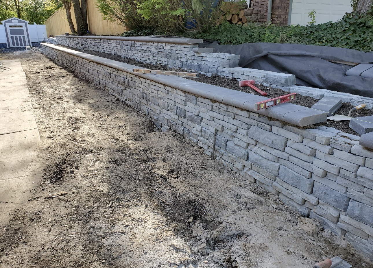 Retaining wall under construction with levels set on freshly laid capstones